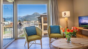 A hotel room with a large window offering a mountain view, two armchairs, a round wooden table with a vase of flowers, and a television on the wall. - SWISSPEAK Resorts Meiringen by Interhome (Meiringen)