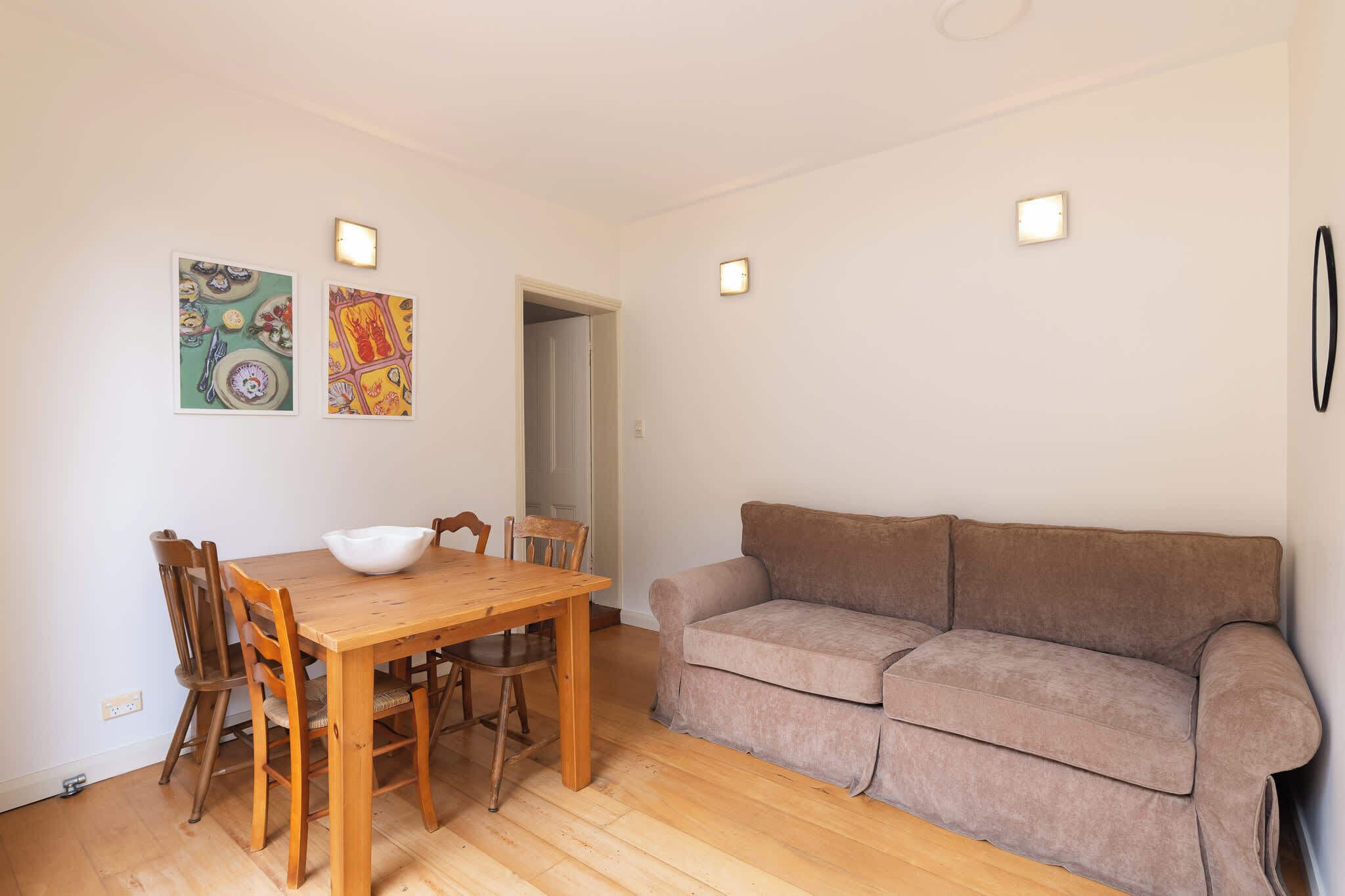 Een eetgedeelte met een houten tafel en stoelen, een beige bank en twee wandlampen.