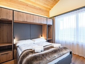 A bedroom with a bed, a fur throw, wooden wardrobe, and a window with sheer curtains. - SWISSPEAK Resorts Thyon 4 Vallées by Interhome (Thyon-Les Collons)