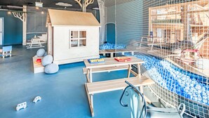 Een speelruimte met een omheinde speelzone, een houten speelhuisje en een tafel met speelgoed.