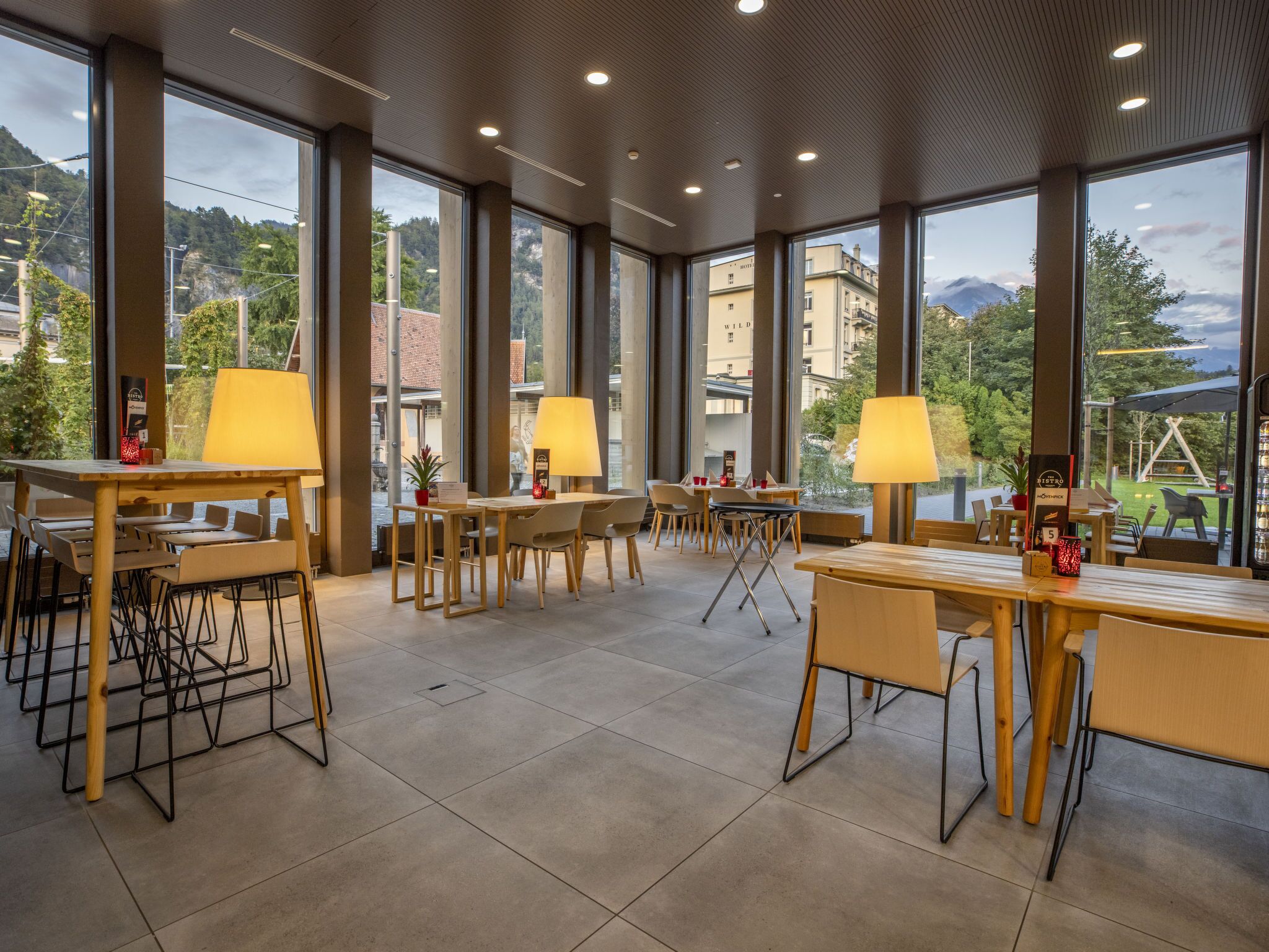 Un vaste espace intérieur doté de grandes fenêtres, de tables, de chaises et de lampes.