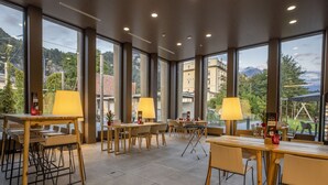 Een ruime binnenruimte met grote ramen, tafels, stoelen en lampen.