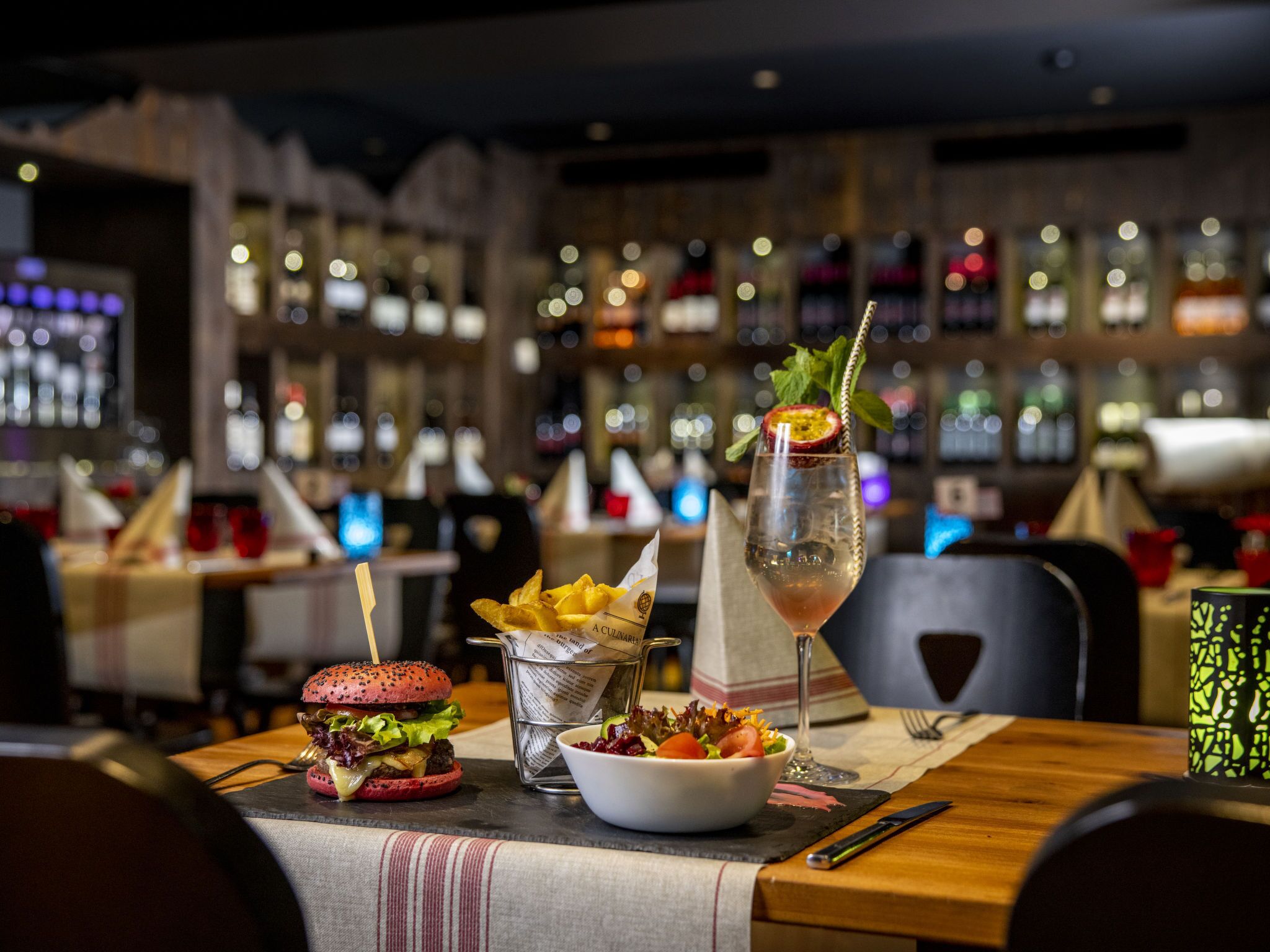 En restaurangmiljö med en hamburgare, en sallad och en cocktail på bordet.