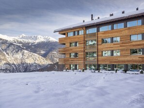 Ein mehrstöckiges Holzgebäude mit großen Fenstern vor einer verschneiten Berglandschaft.