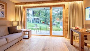 Ein modernes Wohnzimmer mit einer Couch, einem kleinen Tisch und einem Essbereich mit Blick auf einen Garten und Bäume.