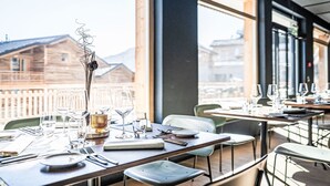 En restaurang med bord som är dukade för middag, stora fönster och utsikt över byggnader och berg.