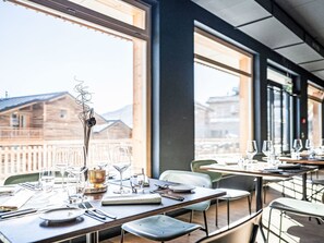 A restaurant with tables set for dining, large windows, and a view of buildings and mountains. - SWISSPEAK Resorts Thyon 4 Vallées by Interhome (Thyon-Les Collons)