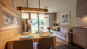 A modern dining area with a wooden table, chairs, and pendant lights. There is a sofa and a kitchen area in the background. - SWISSPEAK Resorts Meiringen by Interhome (Meiringen)