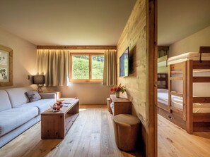 A cozy room with a sofa, a wooden table, a small stool, a bunk bed, and a window with curtains. - SWISSPEAK Resorts Zinal by Interhome (Zinal)