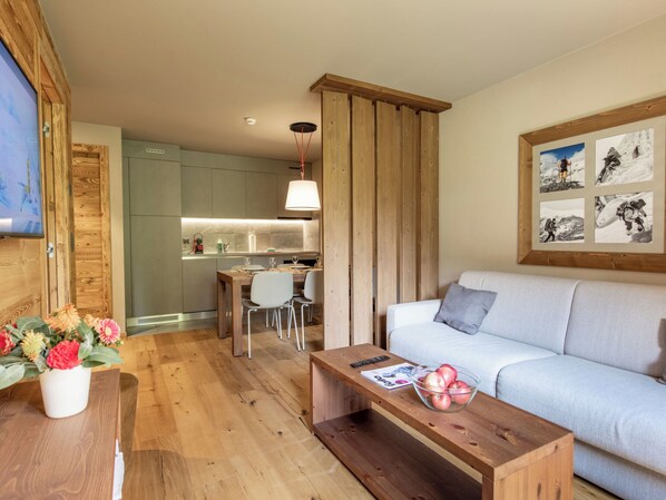A modern living room with a wooden coffee table, a sofa, a dining area with a table and chairs, and a kitchen in the background. - SWISSPEAK Resorts Zinal by Interhome (Zinal)