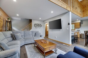 A modern living room with a sectional sofa, a wooden coffee table, and a staircase leading to an upper level. - Poconos Chalet | Hot Tub & Game Room | Sleeps 16 (Blakeslee)