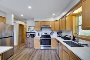 A modern kitchen with wooden cabinets, stainless steel appliances, and a large window. - Poconos Chalet | Hot Tub & Game Room | Sleeps 16 (Blakeslee)