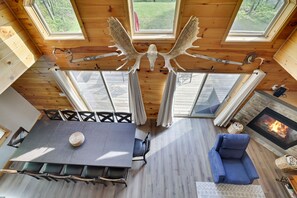 A wooden interior with a dining table, chairs, a sofa, a fireplace, and a ceiling-mounted elk skull. - Poconos Chalet | Hot Tub & Game Room | Sleeps 16 (Blakeslee)