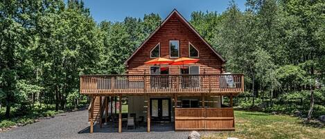 A wooden cabin with a deck, outdoor seating, and a covered area with umbrellas.