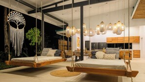 Ein modernes Schlafzimmer mit einer Hängematte, einer Wanddekoration aus Makramee und einem Essbereich mit Korbstühlen.