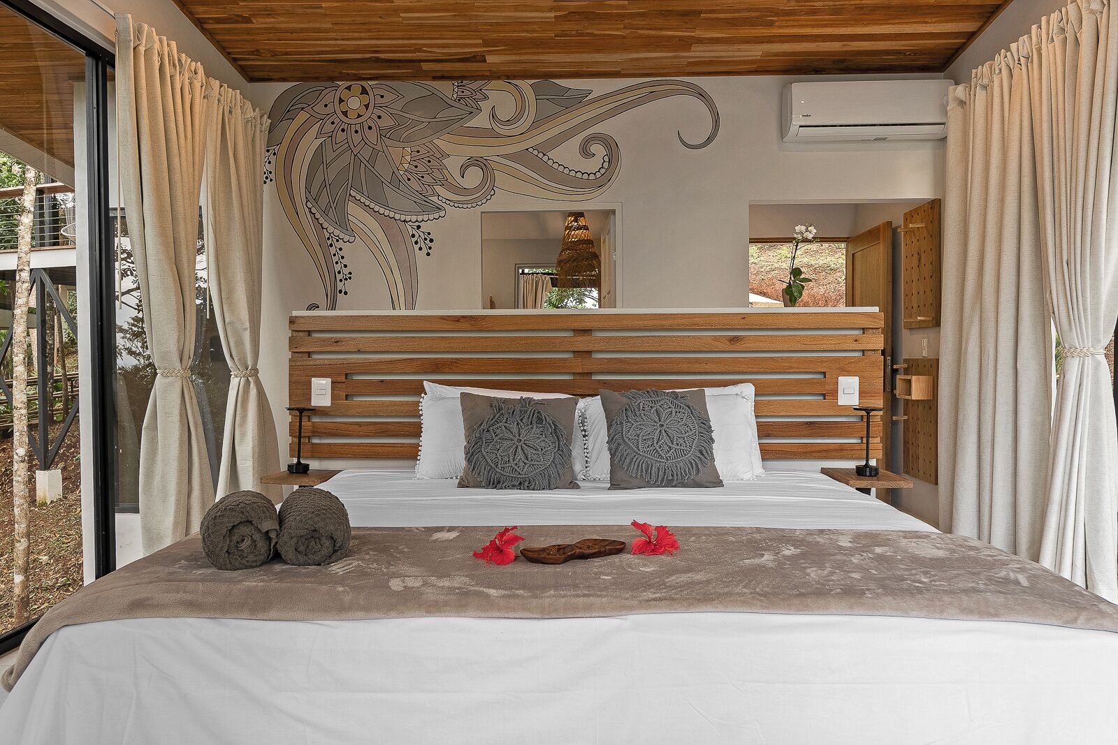 A bedroom with a wooden headboard, a bed with white bedding, decorative pillows, and a view of the outdoors.