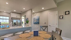 A modern kitchen with a central island, a dining table with placemats, and artwork on the walls. - Bahia Beach Calm Ruskin Retreat (Ruskin)