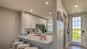 A modern kitchen with white cabinetry, a central island with stools, a built-in microwave, and a large window. - Bahia Beach Calm Ruskin Retreat (Ruskin)