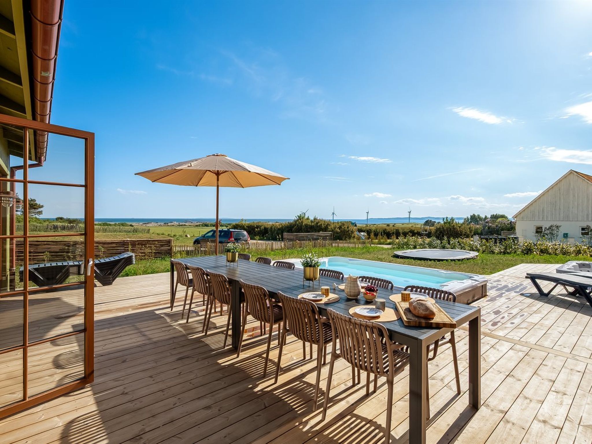 Een houten terras met een pooltafel, buitenmeubels en uitzicht op de oceaan en windturbines.