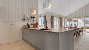 Una cocina moderna con una isla central, luces colgantes y ventanas amplias.