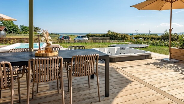 Una terraza con mesa y sillas, un jacuzzi y vista al océano y aerogeneradores.