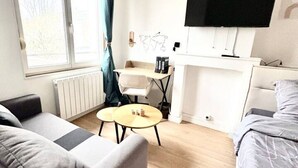 Ett modernt hotellrum med en soffa, ett litet runt bord, en säng, en tv och ett fönster med gardiner.