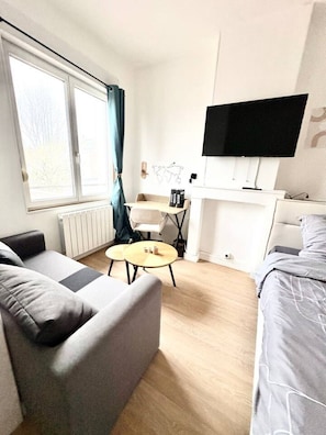A modern hotel room with a sofa, a small round table, a bed, a TV, and a window with curtains. - Studio Dedicated office Autonomous arrival Valenciennes (Valenciennes)