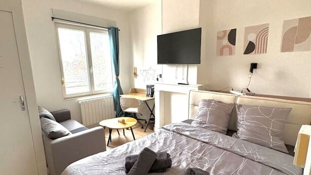 Ett hotellrum med en säng, en tv, ett skrivbord, en stol och ett fönster med gardiner.