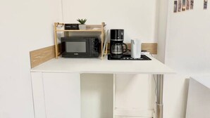 Ett litet pentry med mikrovågsugn, kaffebryggare och en liten hylla med en växt.