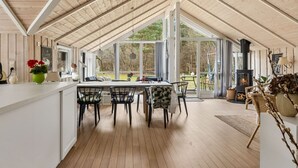 Una habitación amplia con techo alto, ventanas grandes, chimenea y zona de comedor con sillas y mesa.
