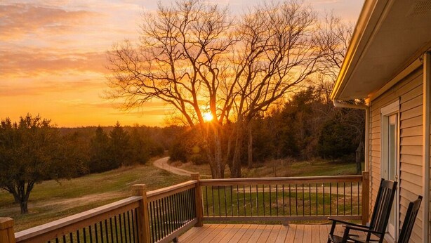 A wooden deck with a railing, a rocking chair, and a view of the sunset. - Country Home-10 ACRES (Towanda)