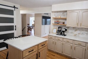 A kitchen with a central island, wooden cabinets, a coffee maker, and a TV mounted above the island.