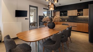 A modern kitchen with dark cabinetry, a marble countertop, and a dining area with a wooden table and patterned chairs. - The Ekfrasis- Mossa Concept Villas (Chania)