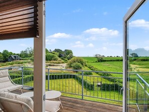 Un balcón con vistas a un paisaje verde, una pequeña mesa y dos sillas.