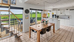 A modern kitchen with white cabinets, a wooden dining table, and a view of a green field. - "Angret" - 380m from the sea by Interhome (Humble)