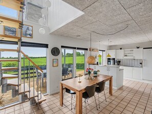 A modern kitchen with white cabinets, a wooden dining table, and a view of a green field.