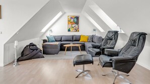 A modern loft with a sloped ceiling, a gray sectional sofa, leather chairs, a small wooden coffee table, and a colorful abstract painting. - "Angret" - 380m from the sea by Interhome (Humble)