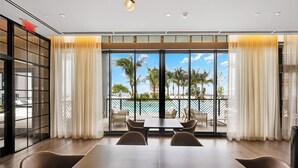 Une chambre d’hôtel moderne dotée d’un grand balcon, d’un coin repas avec tables et chaises, et offrant une vue sur des palmiers et un bâtiment situé de l’autre côté de l’eau.