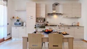 A modern kitchen with light wood cabinets, a central island with seating, and a dining table. - Casa Carla by Interhome (Gravedona)