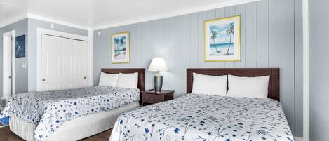 Een hotelkamer met twee bedden, een plafondventilator, een nachtkastje met lamp en ingelijste foto’s aan de muur.