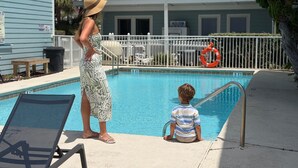 A swimming pool with a lifebuoy, lounge chairs, and a building with balconies in the background.