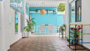 A corridor with tiled flooring, white walls, and a blue accent wall. There are potted plants, a hanging wicker light fixture, and a rack with colorful balls. - PalmHousePR Luxury Tropical Villa w/ Private Pool Perfect for Groups San Juan (San Juan)