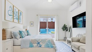A bedroom with a bed, bedside table, TV, and a view of a balcony. - PalmHousePR Luxury Tropical Villa w/ Private Pool Perfect for Groups San Juan (San Juan)