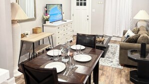 A dining area with a wooden table set for four, a television, a white door, and a living room with a sofa and a lamp. - Entire Private Home • Sleeps 6 • Prime Salisbury Location (Salisbury)