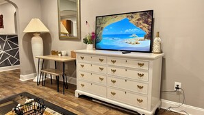 A living room with a television, a white cabinet with gold handles, a lamp, and a dining area. - Entire Private Home • Sleeps 6 • Prime Salisbury Location (Salisbury)