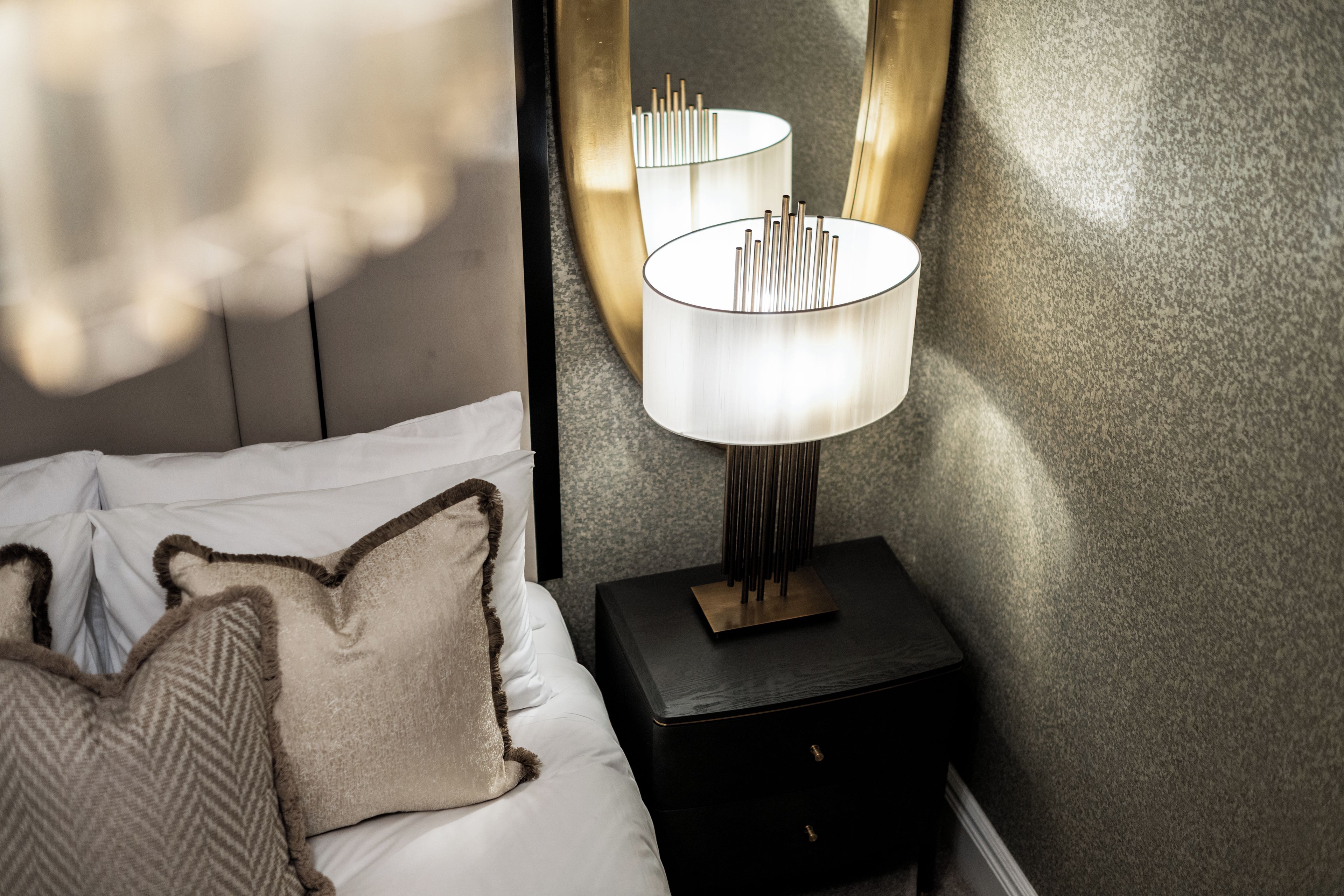 A neatly made bed with white linens and two decorative pillows, a modern bedside table with a lamp, and a textured wall.
