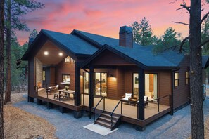Uma cabana de tronco moderna com varanda, área de estar externa e escadaria que leva à entrada.