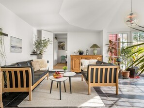 Een moderne woonkamer met een zithoek, een salontafel en een eettafel. Links staat een plant en rechts een lamp.