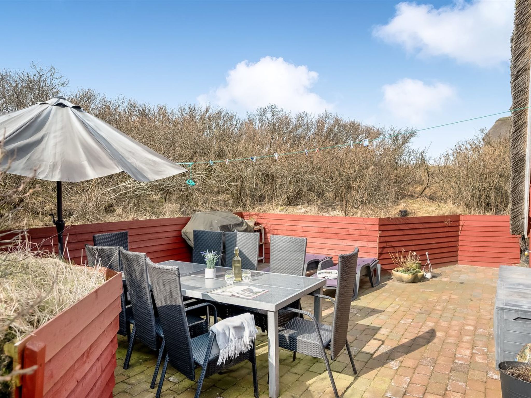 Eine Terrassengruppe im Freien mit Tisch, Stühlen, einem Grill und einem roten Holzzaun.
