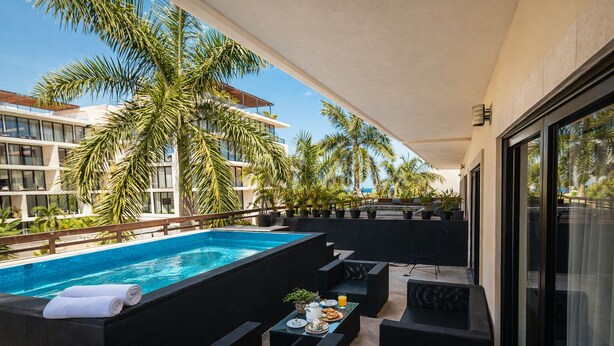 A rooftop pool area with a view of palm trees and a modern building in the background. - Master Suite with private Pool in Aldea Thai (Playa del Carmen)